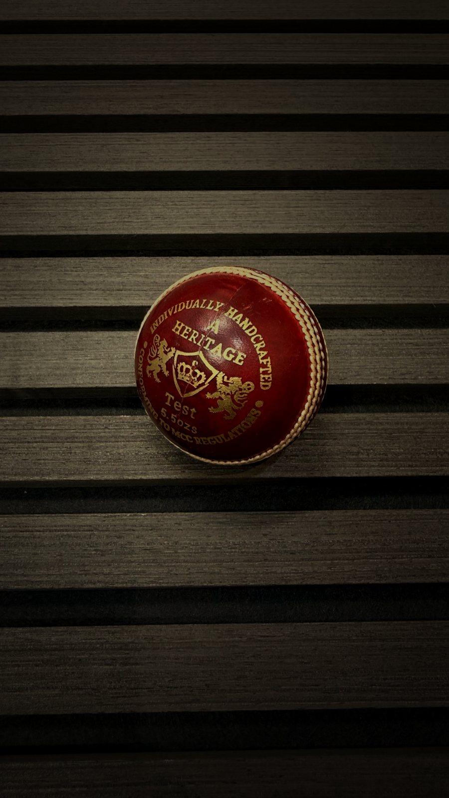 Heritage Test cricket ball on a dark wood slat surface