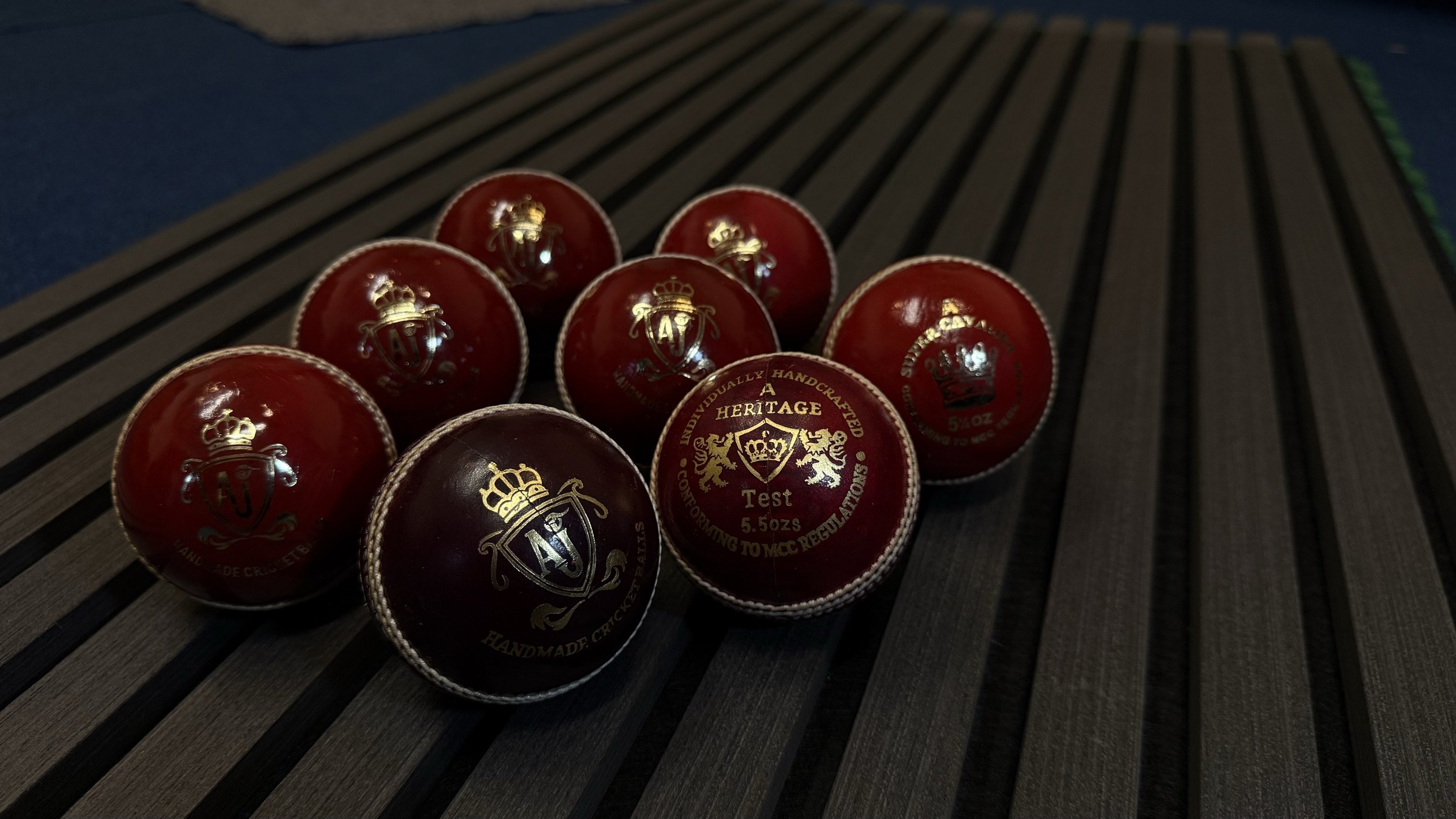 AJ hand stitched cricket balls resting on dark wooden slats