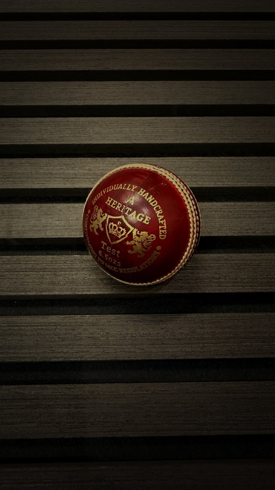 Heritage Test cricket ball on a dark wood slat surface